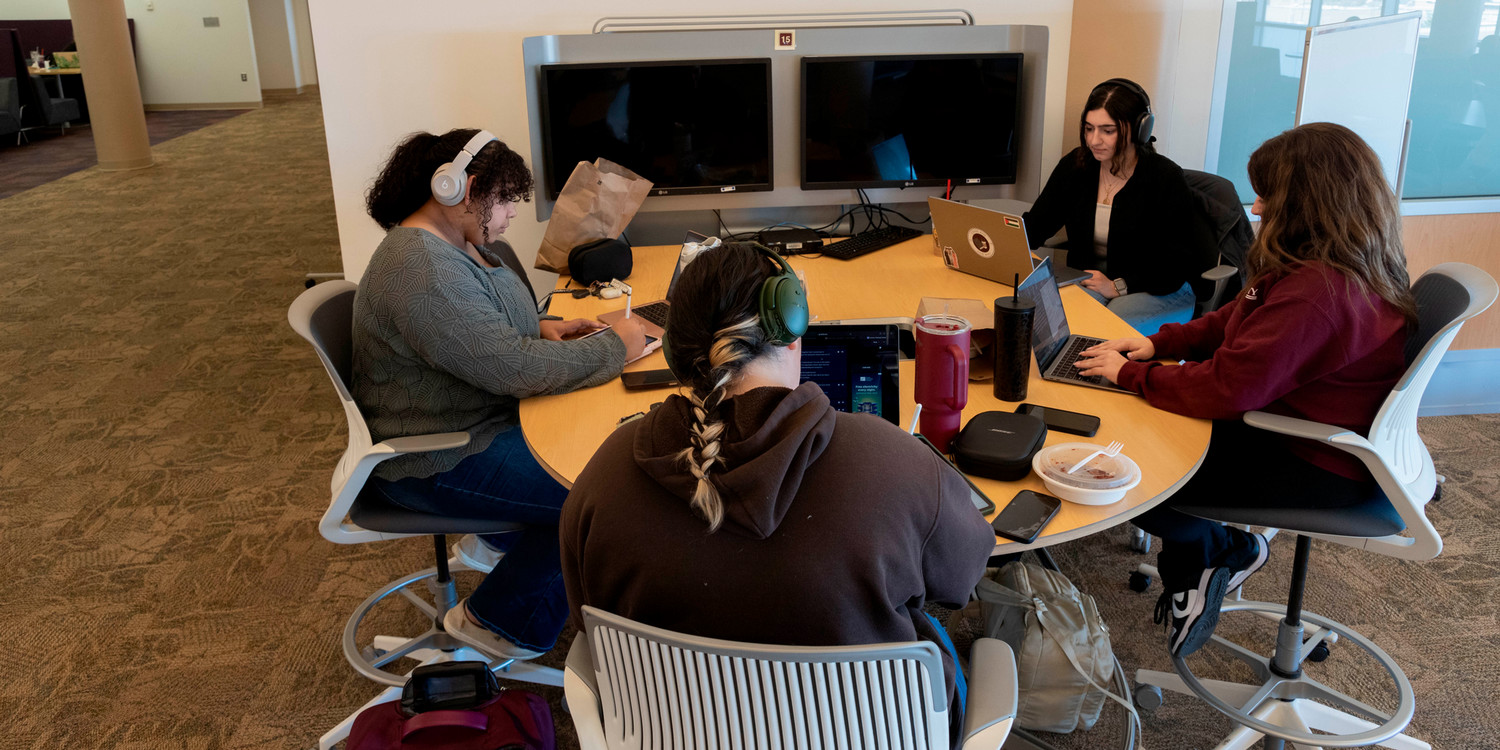 four women gathered around a table in the library studying